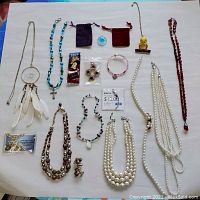 Top-down view of assorted necklaces, pendants, pins, and earrings laid flat on white surface.