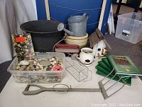Photo showing entire lot with books, planters, birdhouse, decorative wagon and house, metal bucket/watering can, metal planter, rock collection, decorative pitchfork, clothesline hanger, and garden pitchfork tool.