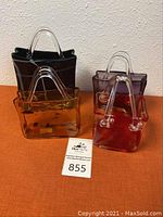 Photo of four blown glass baskets shaped like handbags in black, amber, brown and red with clear handles