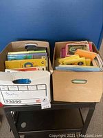 Two cardboard boxes filled with a variety of children’s books arranged upright showing colorful spines and covers.