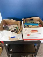 Two large cardboard boxes filled with multiple children’s books packed inside. Books include storybooks, learning books, and workshop booklets.