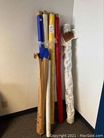 Seven bolts of fabric in various colors and one striped pattern leaning against a wall showing approximate length and wrapping.