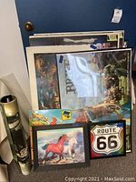 Photo showing framed holographic running horses art, framed holographic Route 66 sign art, and several stacked posters including Brave, Billy Joel, and Route 66.