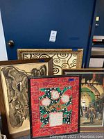 Four large framed artworks leaning against a dark blue wall with mixed subjects and styles as described.