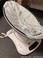 Full view of 4 Moms Mamaroo baby swing seat in light gray fabric, showing power cord and strap.