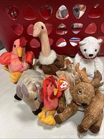 Assorted stuffed animals including Beanie Babies, a Hilfiger 2000 bear, and Ichiro bear in front of red plastic laundry basket