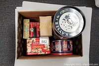 Photo showing the assortment of tins packed in a cardboard box, displaying size and shape variety.