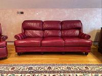 Front view of the red leather sofa showing three seat cushions and rolled arms with nailhead trim.