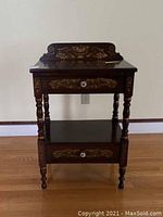 Front view of the L. Hitchcock side table showing two drawers and floral decoration with turned legs.