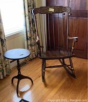 Full view of the L. Hitchcock style wooden rocking chair with decorative back panel and armrests, showing furniture wear and scratches