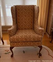 Front and side views of a wingback chair featuring floral upholstery, visible stains, and signs of wear. Chair has curved wooden legs and typical wingback design.