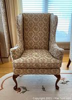 Full front view of the wingback chair showing floral upholstery, cushioned seat and back, and wooden legs.