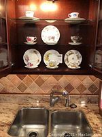 Cabinet display showing eight teacups and saucers along with eight dessert plates featuring floral patterns.