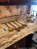 Photo of brass kitchen utensil wall hanging, brass ducks, bowl, and candle holders on countertop.