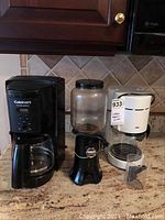 Overview of the lot showing Cuisinart coffee maker, KitchenAid coffee grinder in center, and Braun coffee maker on right.