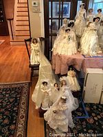 Full view of the bridal doll collection displayed on furniture and adjoining floor area, showing multiple dolls in wedding gowns of various styles and sizes.