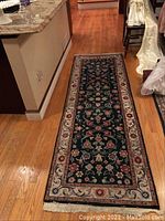 Long runner rug laid out on hardwood floor, showing full length floral pattern and beige border with fringed end.