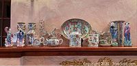 Wide shot of all porcelain items including figurines, vases, jars, teapot and platter arranged on shelf