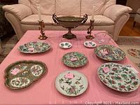 All items arranged on pink tablecloth including decorative plates, candlesticks, metal bowl, and crystal bowl