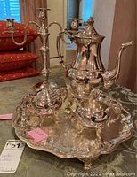 Three-piece Sheridan silver on copper coffee service set including coffee pot, sugar bowl, and creamer on matching silver plate tray, shown with red cushions in background