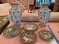 All six items on pink tablecloth: two hexagonal vases at back, four plates front