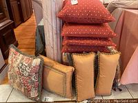 Stack of four red square throw pillows with light dot pattern and three smaller gold pillows with dark rope trim and one floral pillow in front