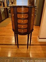 Front view of standing jewelry cabinet on four slender turned legs showing five burl veneer drawers and dark wood finish.