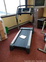 Full view of NordicTrack C2270 treadmill in an office/workshop setting showing black running belt, silver side rails, and user manual on the treadmill bed.