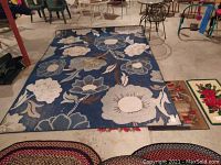 View of full indoor/outdoor rug with blue background and flower pattern laid out on concrete floor.