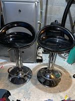 Two black and chrome adjustable height bar stools shown from the front with seats and bases visible.