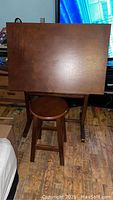 Full front view of drafting table with wooden stool placed in front.