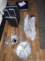 Full view of subwoofer, satellite speakers, metal pedestals wrapped in plastic, cables, and manuals arranged on floor