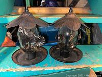 Two bronze and glass bird feeders with flower petal shaped tops and leafy vine designs on glass, shown side by side.