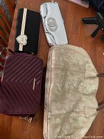 Photo showing four assorted ladies purses including large gold purse, maroon quilted crossbody and wallet, silver clutch with rhinestone, and black wallet with heart detail