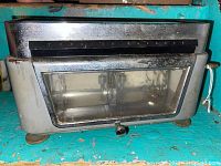 Front view of the antique torsion balance scale showing the metal casing and glass window with visible internal balance mechanism.