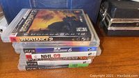 Stacked seven PS3 game cases showing top game Resistance 2 and clearly visible titles NHL 09, Gran Turismo 6, Dragon Age Origins, XCom Enemy Unknown, Battlestorm Limited Edition, and Fallout New Vegas.