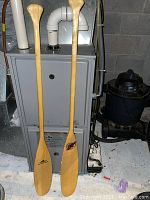 Two wooden paddles standing upright in front of a furnace, showing full length and logos on blades