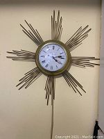 Front view of sunburst design electric wall clock showing circular face with Roman numerals and metal rays extending outward.