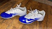 Pair of boys youth soccer cleats in blue and white by Nike on hardwood floor, size 5.5 US.