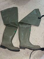 Side and front view of dark green tall fishing boots showing long legged design and textured sole.