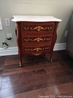 Front view of wooden table showing three drawers, marble top, gilt accents and cabriole legs