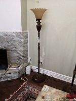 Full view of the tall floor lamp placed near a wall with stonework and hardwood floor visible.