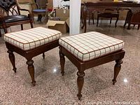 Pair of square wooden footstools with cushions on showroom floor
