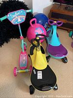 Various children's ride-on toys displayed on carpet including scooter, two wiggle cars, and two hopper balls.