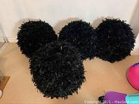 Four black feathered spherical decorative balls arranged on a carpeted floor.