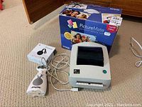 Epson PictureMate printer with original box, Zebra label maker with cables, and Google Chromecast box on carpeted floor.