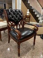 Front view of wooden framed faux leather chair showcasing tufted backrest and cushioned seat with carved armrests and legs.