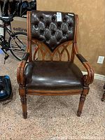 Front view of the faux leather chair showing tufted backrest and curved wooden arms.