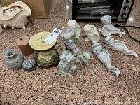 Photo showing a collection of ceramic decorative items including vases, candle holders, boxes, and porcelain figurines of cupids and animals, arranged on countertop.