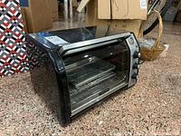 Black and Decker toaster oven showing front and side view, including control knobs and interior with metal rack and glass baking pan.